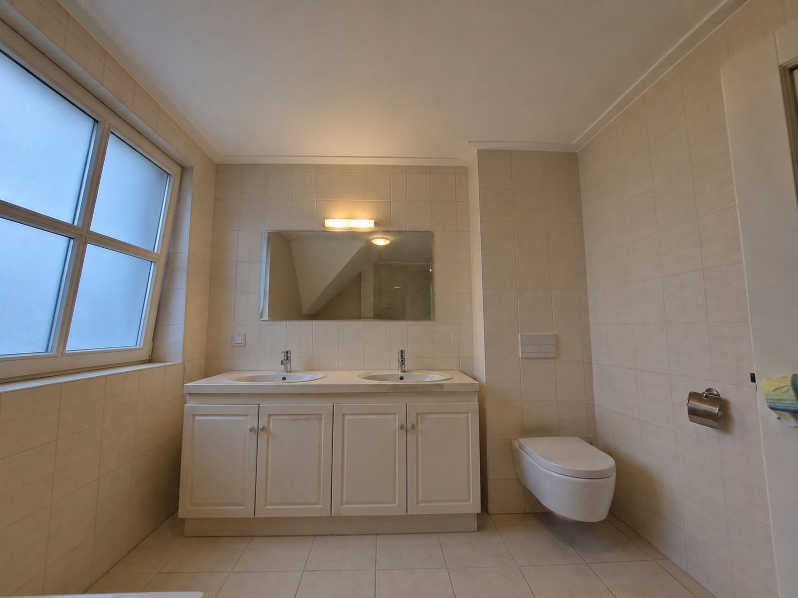 Ruime badkamer vóór de renovatie — gedateerd beige met oud meubel