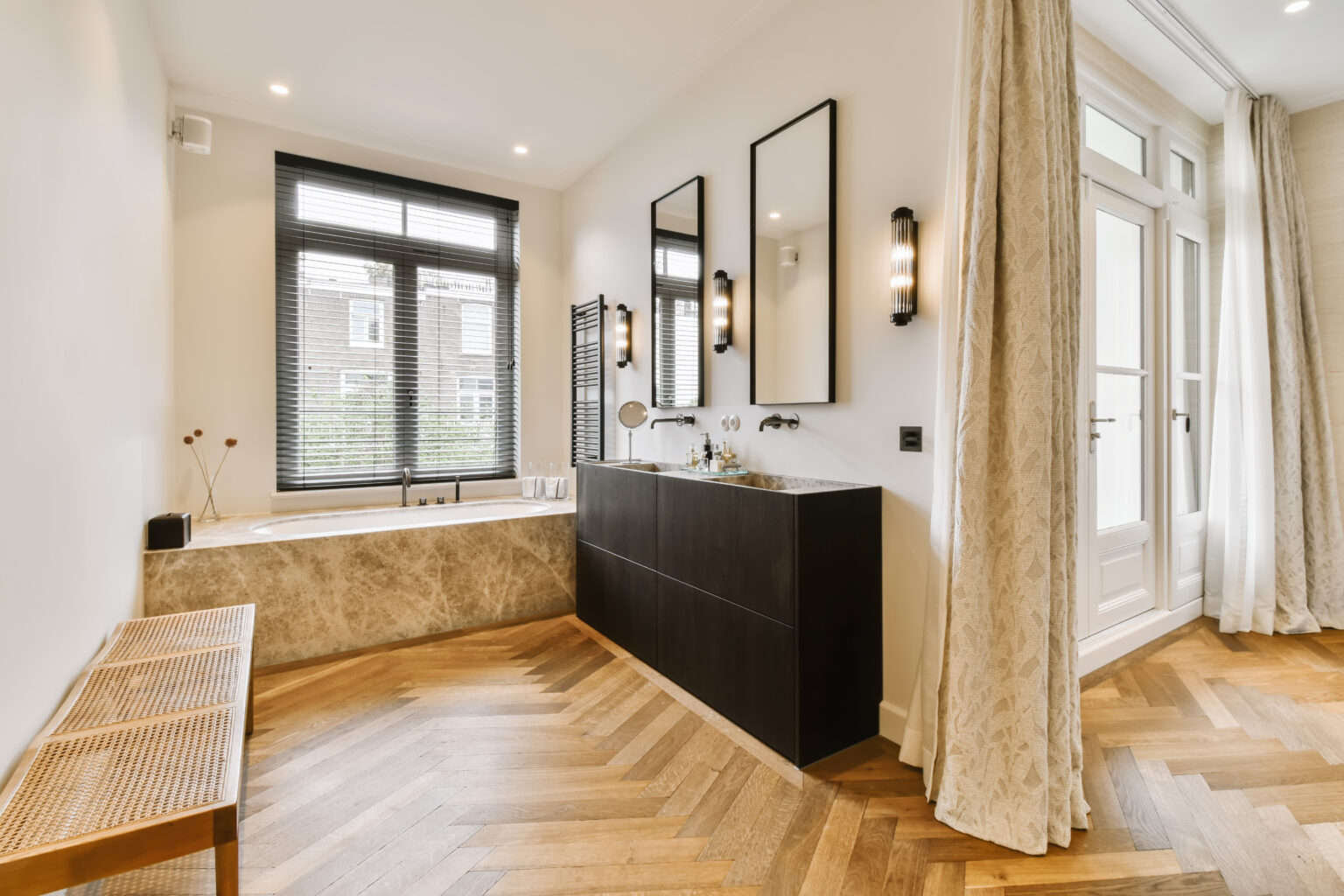 a modern bathroom with wood flooring and black cabinetd bathtub in the center of the room is a wooden bench