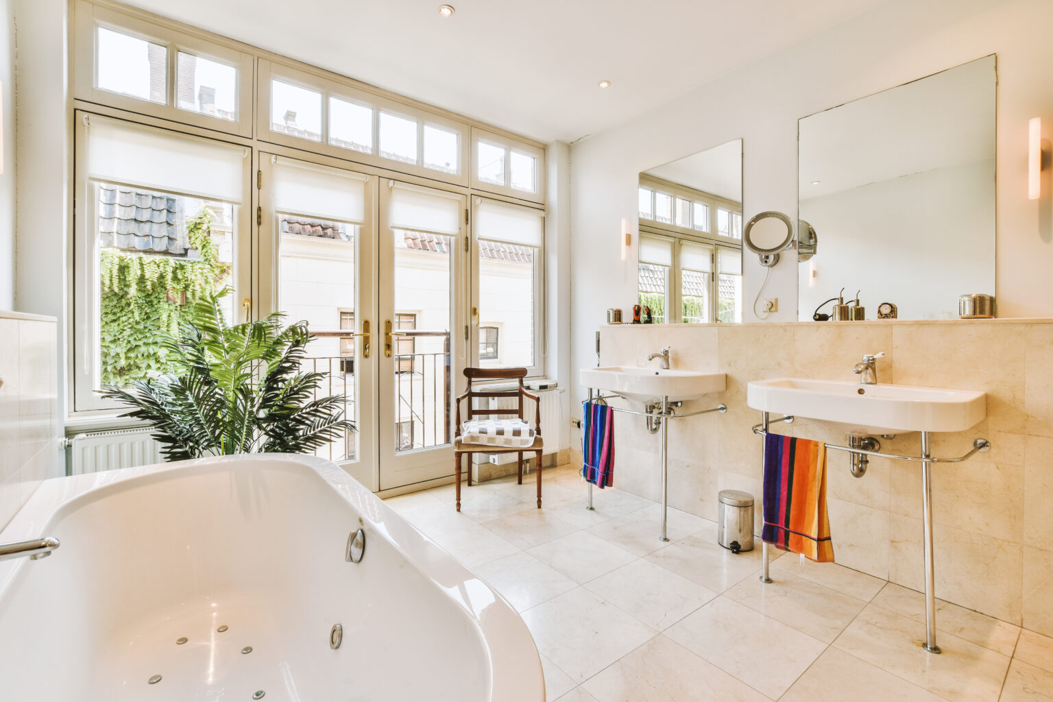 Sinks with mirrors and clean bathtub located near shower box with glass door in modern bathroom with white tiled walls